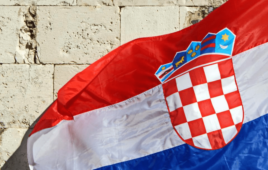 Croatian flag waiving, with a stone wall showing in the background.