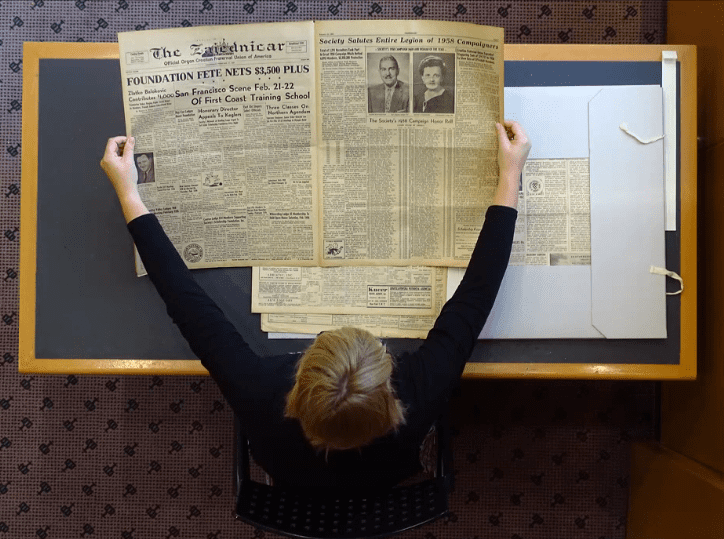 Librarian spreading historic newspapers in a library reading room.