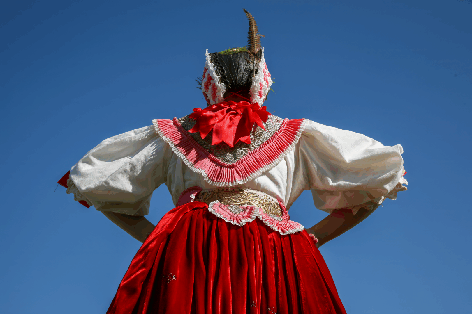 Ženska folklorna nošnja snimljena odozdo na pozadini vedroga plavog neba.