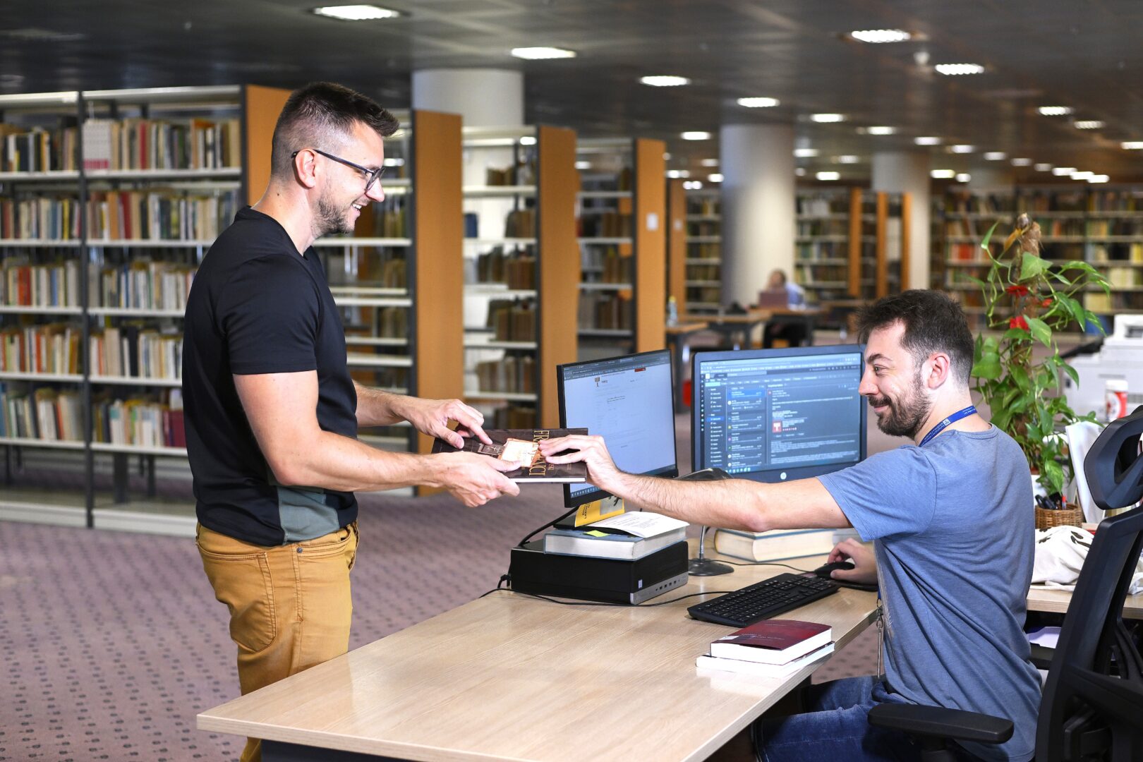 Young male NSK user returning an overdue loan to a male member of NSK staff at a loan desk in one of NSK’s reading rooms.